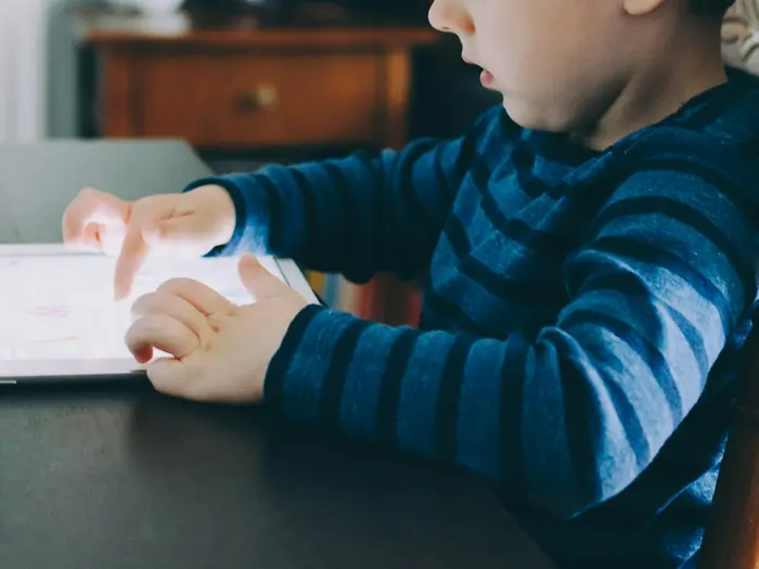A young boy working on a tablet at the kitchen table